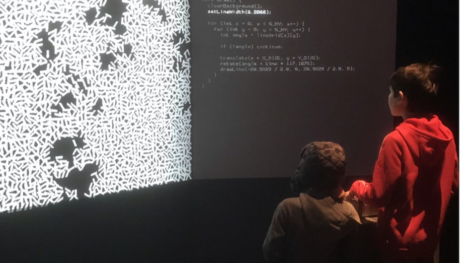 people looking at a large display of generative art next to its accompanying code